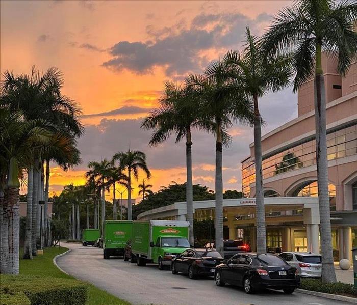 Several SERVPRO trucks sit in front of a commercial building, as the sun sets in the background